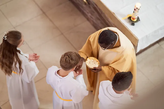 Ein Pfarrer verteilt Hostien an drei Ministranten in der Kirche Salvator